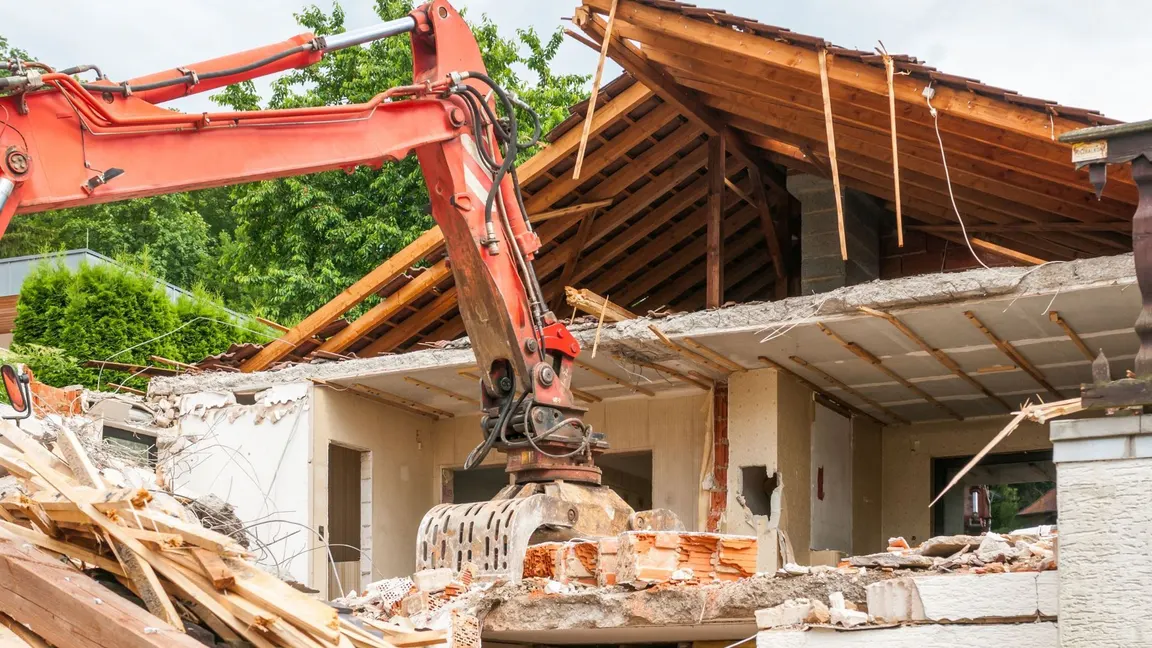 Heavy machinery demolishing a house on a residential lot