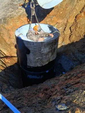 Excavator lowering a concrete manhole section into place