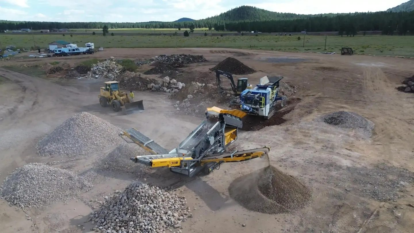 Mobile crushers and a loader working a crushed-stone processing yard