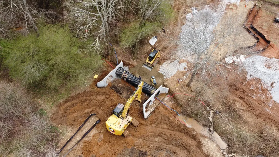 Aerial view of an excavator setting a large culvert pipe