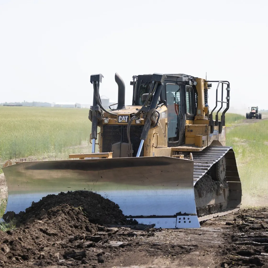 Bulldozer spreading topsoil across an open field