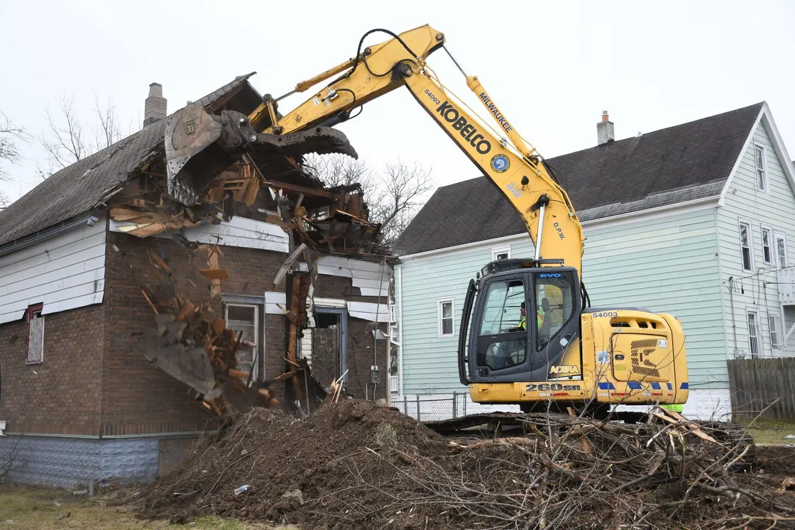 Excavator pulling down the wall of a house at a demolition site