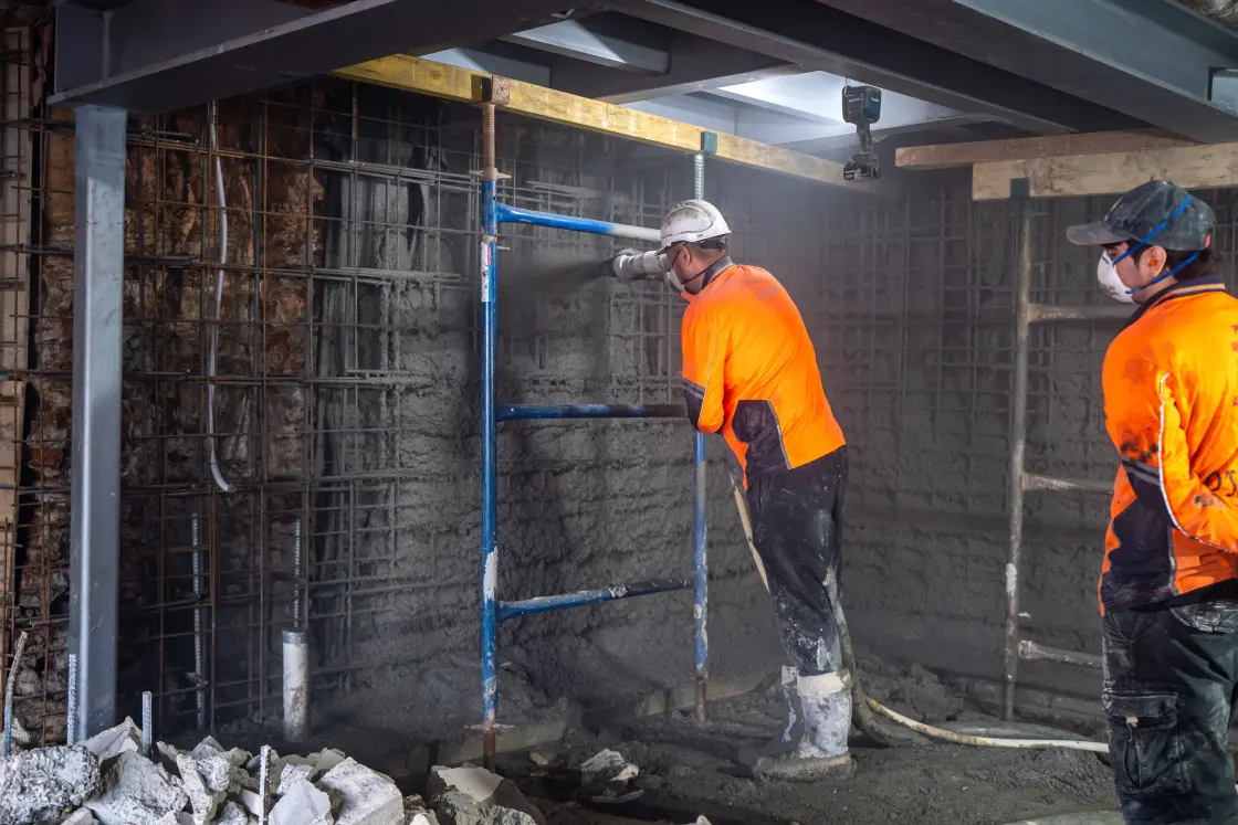 Workers waterproofing a poured concrete foundation wall